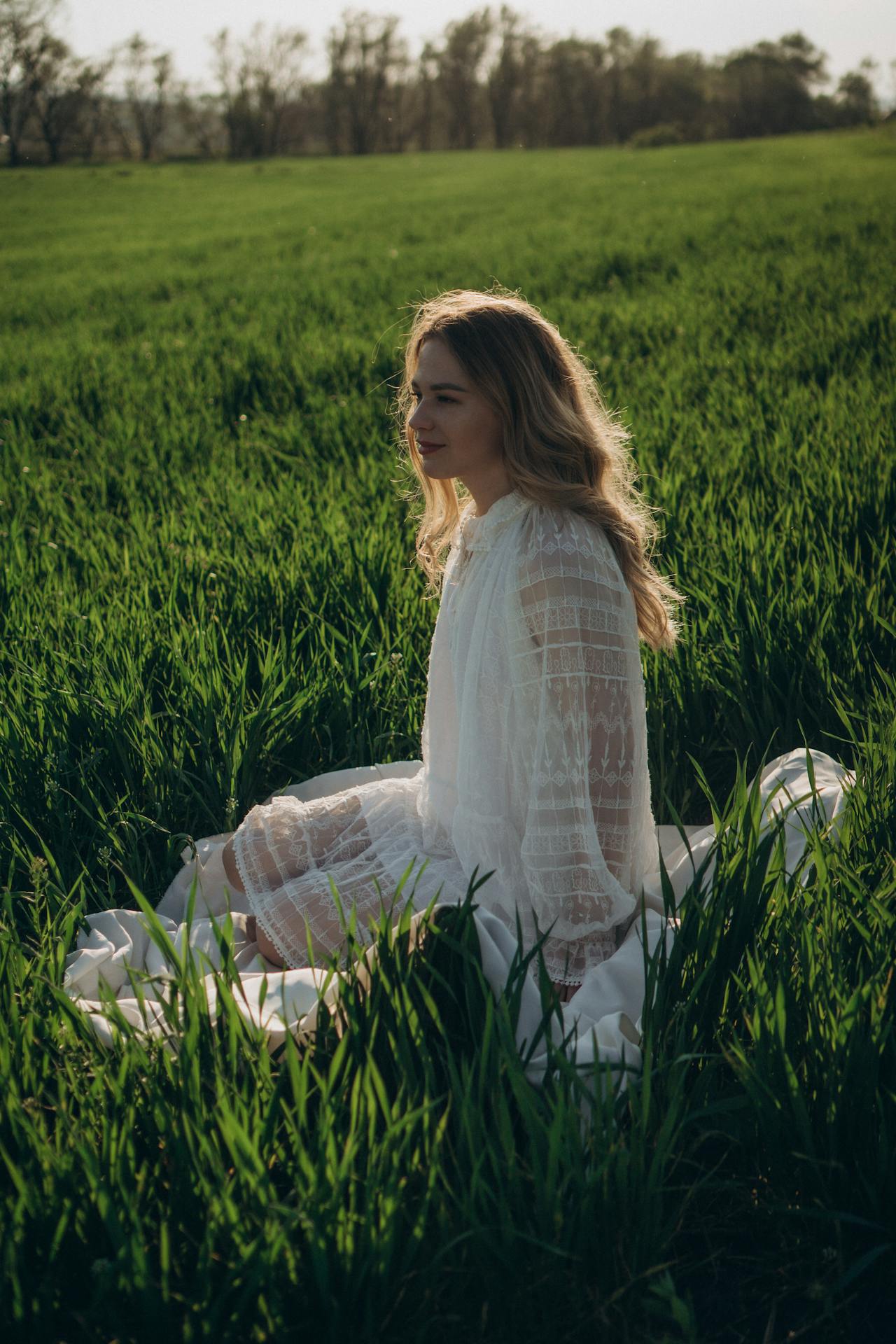 A Woman in White Dress Sitting on Green Grass Field A woman in a white dress sitting on a green grass field
