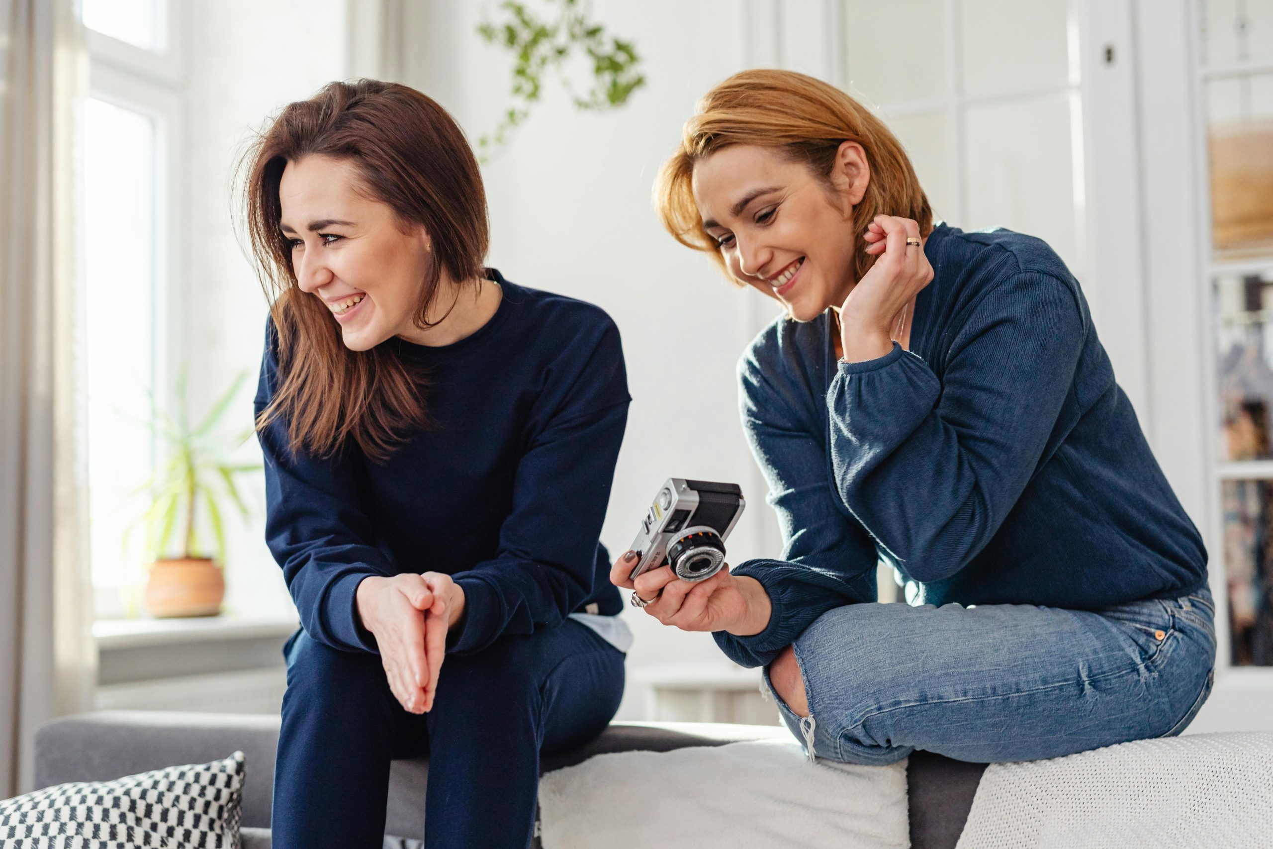 pexels-karola-g-6135162 Two women sit together in a sunlit living room, laughing while looking at a camera
